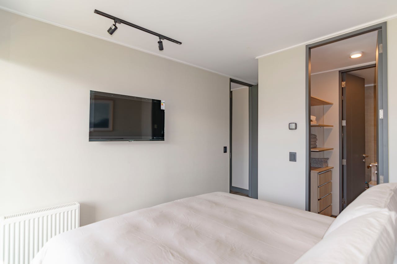 services-03 A modern bedroom featuring a cozy bed, wall-mounted TV, and minimalist decor.